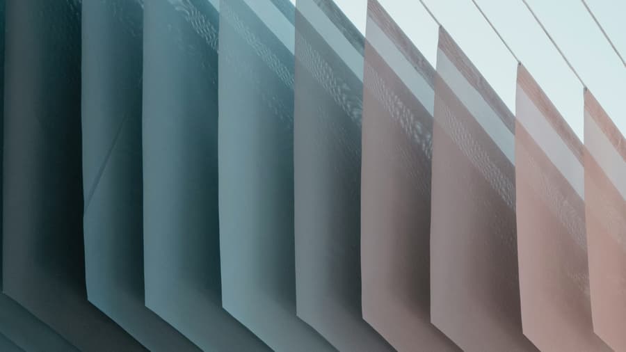 Close-up of overlapping vertical panels in blue and pink light beneath a pale sky.